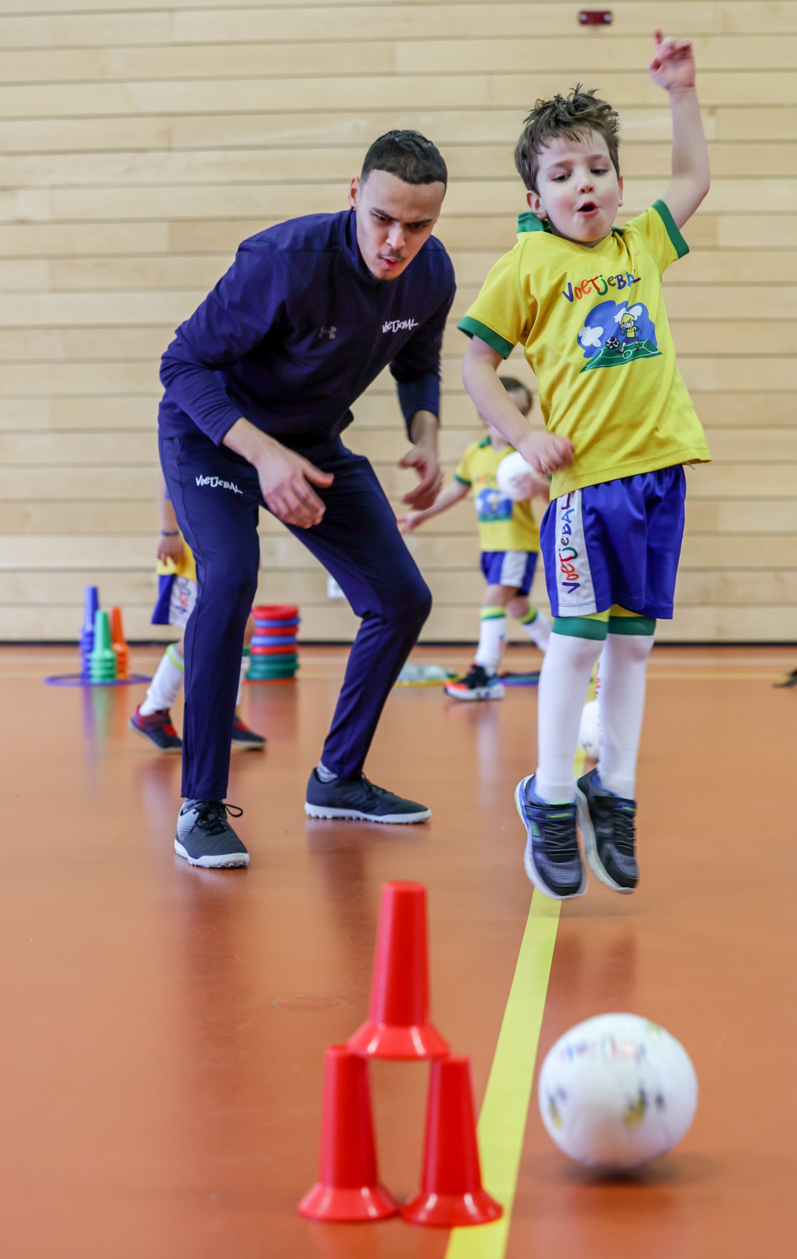 Trainer begeleidt een lachend kind in Voetjebal-shirt tijdens een training